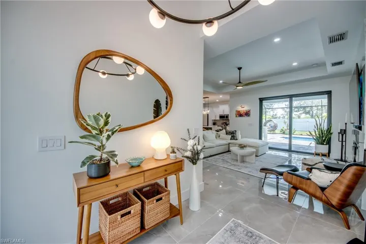 Tiled living room featuring a raised ceiling and ceiling fan with notable chandelier