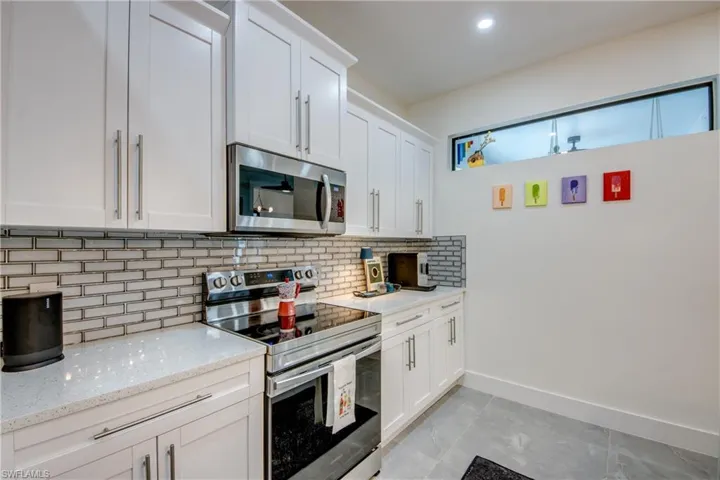 Kitchen with backsplash, appliances with stainless steel finishes, white cabinetry, and light tile floors