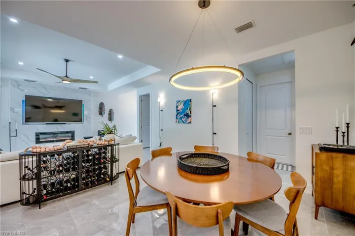 Dining room featuring a tray ceiling, a fireplace, light tile flooring, and ceiling fan