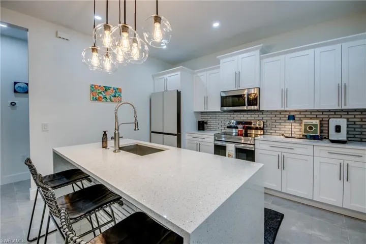 Kitchen featuring tasteful backsplash, an island with sink, stainless steel appliances, pendant lighting, and light tile floors