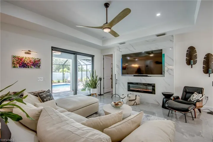 Tiled living room with ceiling fan, a raised ceiling, and a high end fireplace