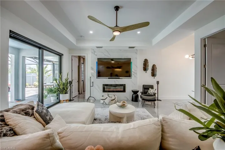 Living room with a high end fireplace, a raised ceiling, and ceiling fan