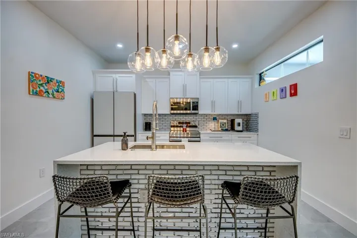 Kitchen featuring hanging light fixtures, a center island with sink, tile floors, a kitchen bar, and appliances with stainless steel finishes