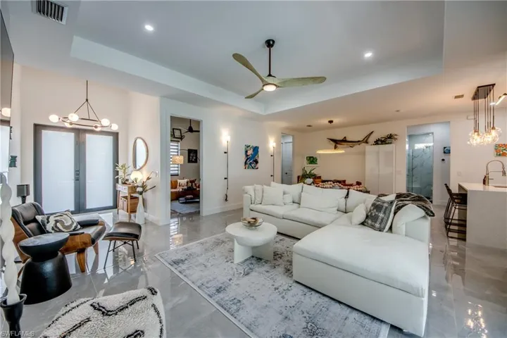 Tiled living room featuring sink, french doors, a raised ceiling, and ceiling fan with notable chandelier