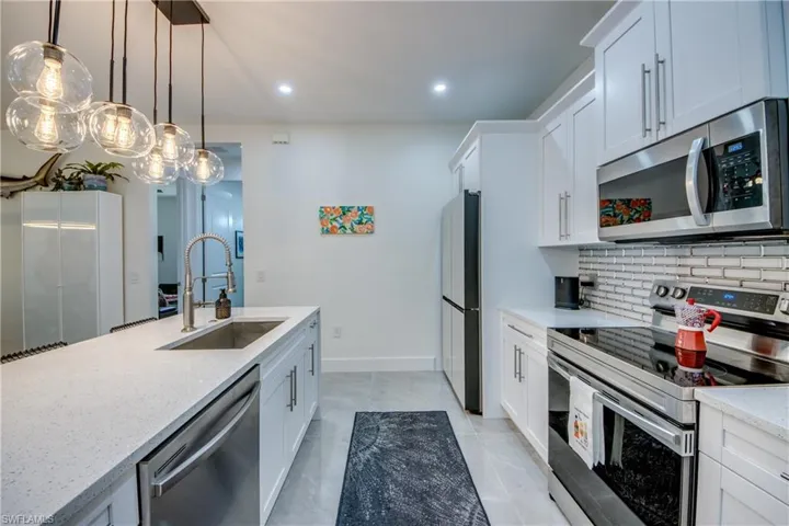 Kitchen featuring light tile flooring, backsplash, hanging light fixtures, sink, and appliances with stainless steel finishes