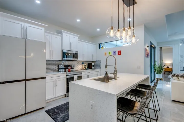 Kitchen with stainless steel appliances, hanging light fixtures, white cabinetry, and light tile floors
