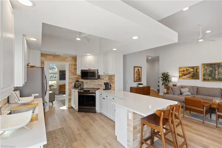 Kitchen featuring kitchen peninsula, appliances with stainless steel finishes, a breakfast bar, white cabinets, and light wood-type flooring