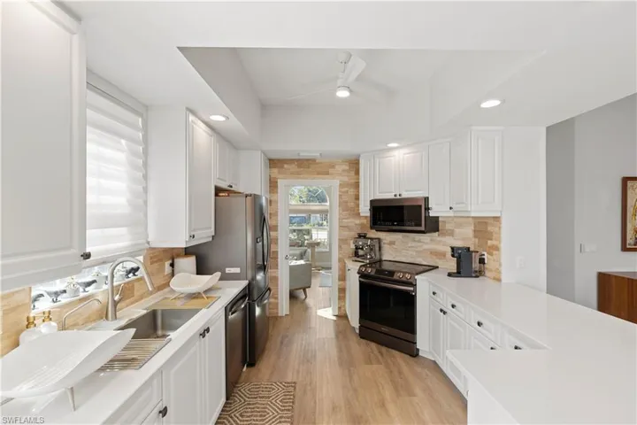 Kitchen with new ceiling fan, farmhouse sink, stainless steel appliances, backsplash, and white cabinets