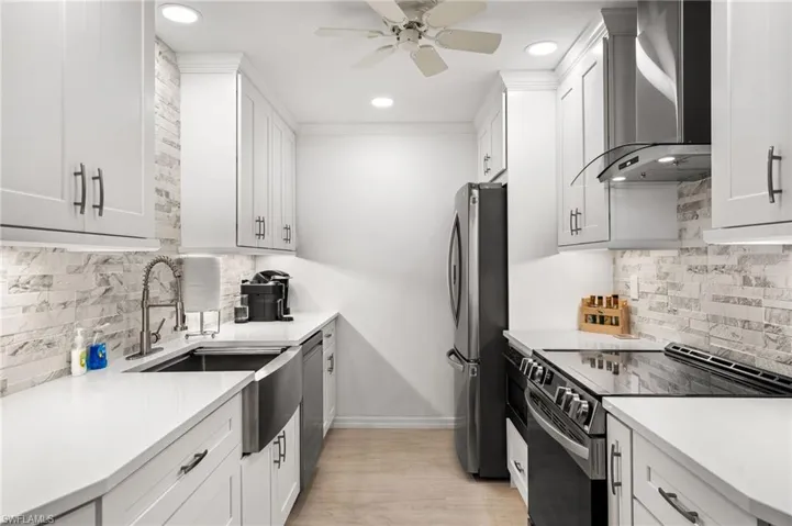 Kitchen with sink, white cabinetry, wall chimney exhaust hood, and stainless steel appliances