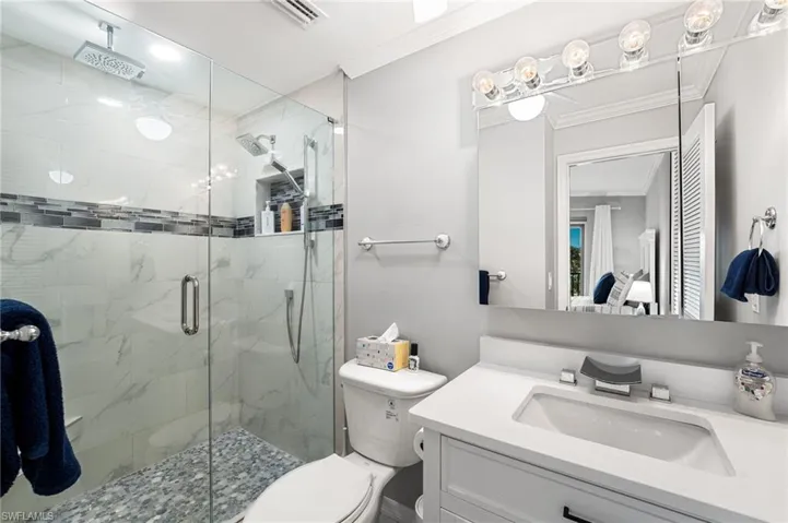 Bathroom with an enclosed shower, vanity, ornamental molding, and toilet
