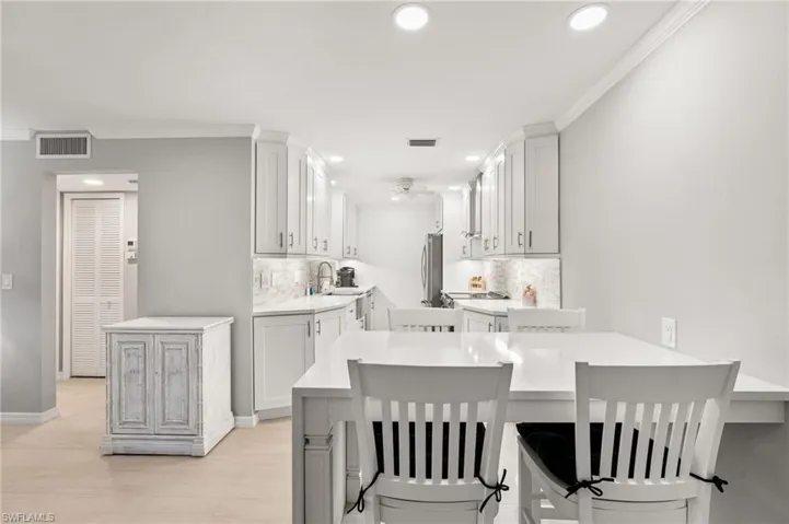 Kitchen featuring white cabinetry, kitchen peninsula, a breakfast bar area, backsplash, and stainless steel refrigerator