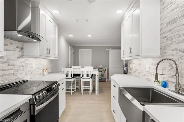 Kitchen featuring white cabinets, wall chimney range hood, tasteful backsplash, sink, and stainless steel electric range
