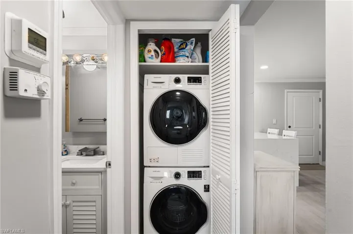Laundry area featuring stacked washer / dryer, sink, crown molding, and light hardwood / wood-style floors