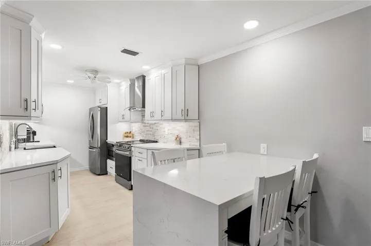 Kitchen with wall chimney range hood, sink, stainless steel appliances, and white cabinetry