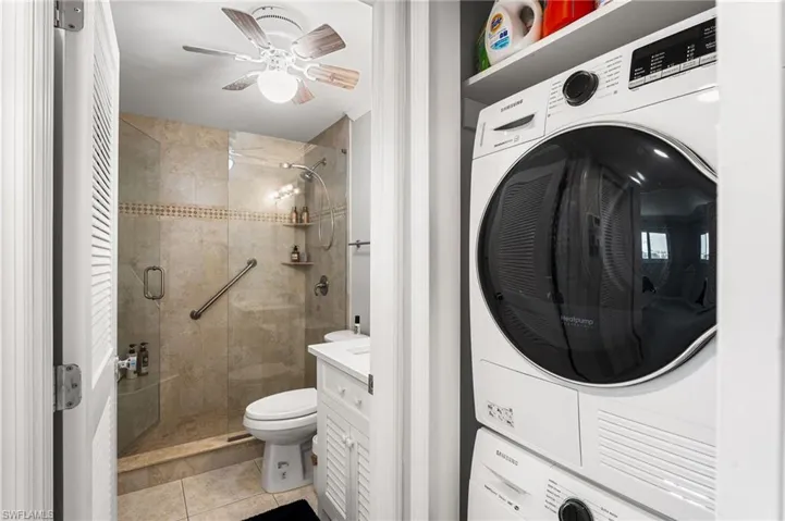 Clothes washing area with light tile patterned floors and stacked washing maching and dryer