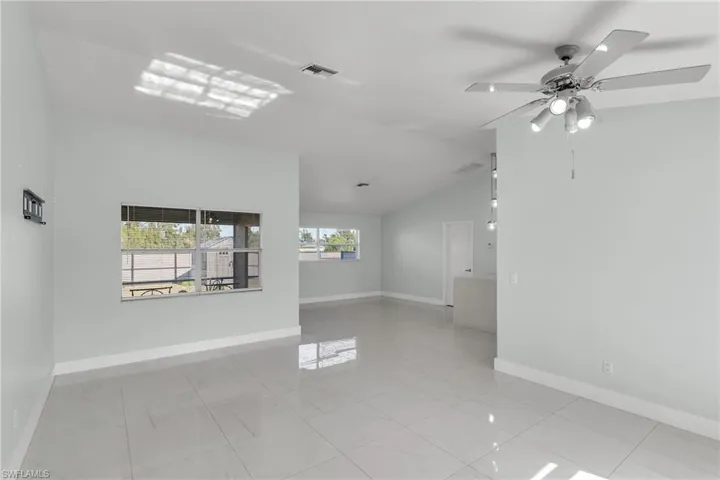 Tiled empty room featuring ceiling fan, a wealth of natural light, and lofted ceiling