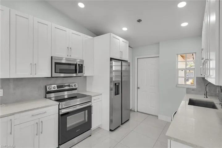 Kitchen with stainless steel appliances, light stone countertops, sink, white cabinetry, and tasteful backsplash