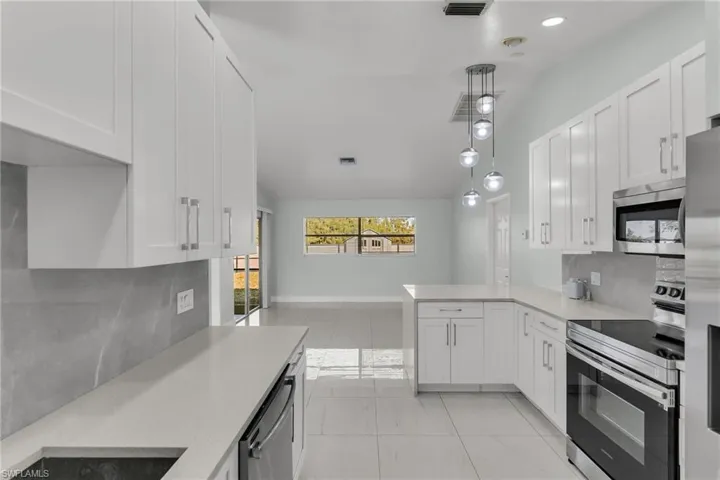 Kitchen with kitchen peninsula, white cabinets, appliances with stainless steel finishes, and pendant lighting