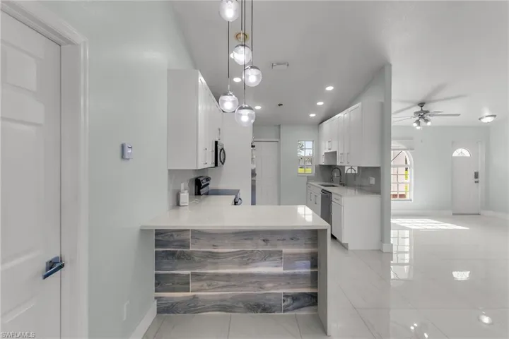 Kitchen with sink, white cabinetry, light tile patterned floors, kitchen peninsula, and appliances with stainless steel finishes
