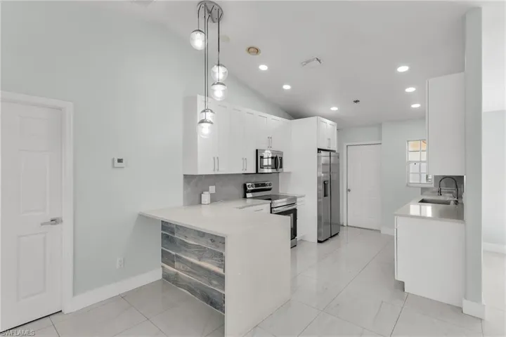 Kitchen featuring sink, white cabinetry, vaulted ceiling, hanging light fixtures, and appliances with stainless steel finishes