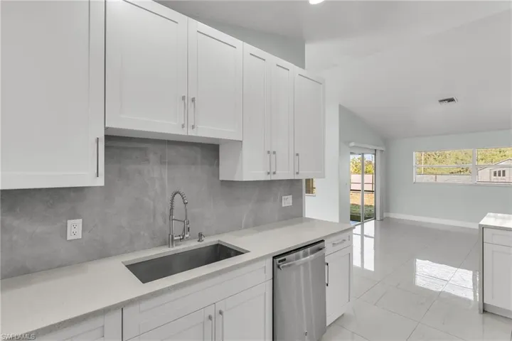 Kitchen featuring sink, white cabinets, stainless steel dishwasher, and lofted ceiling