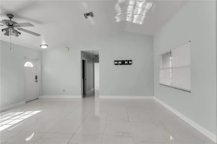 Unfurnished room featuring ceiling fan with notable chandelier, lofted ceiling, and light tile patterned floors