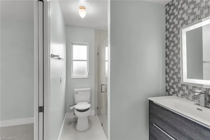 Bathroom with vanity, a shower with shower door, tasteful backsplash, and toilet