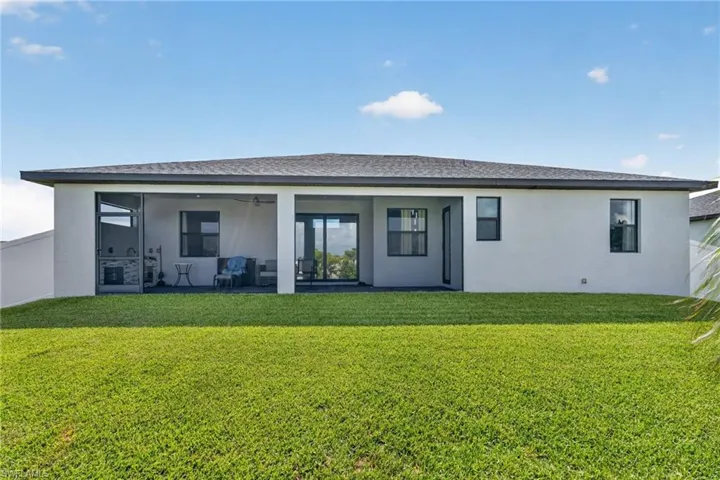 Expansive green lawn with a contemporary single-story home featuring a covered patio, screened-in outdoor kitchen, and dark-framed windows