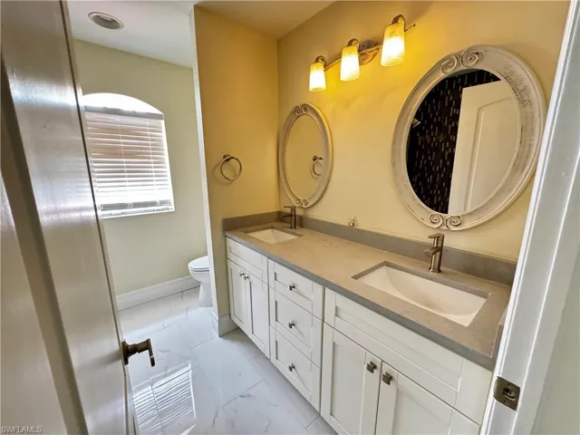 Full bathroom featuring marble look tiles, double vanity, and toilet