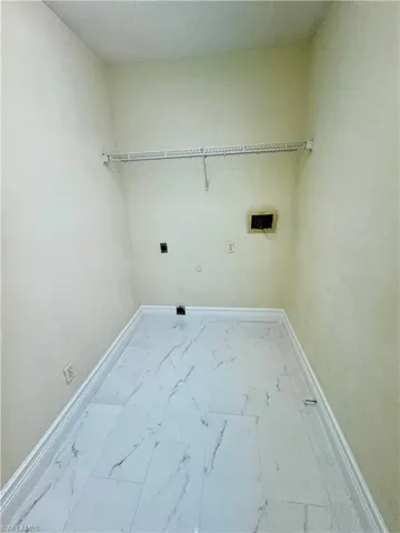 Washroom with electric dryer hookup, baseboards, marble look tiles, and washer hookup