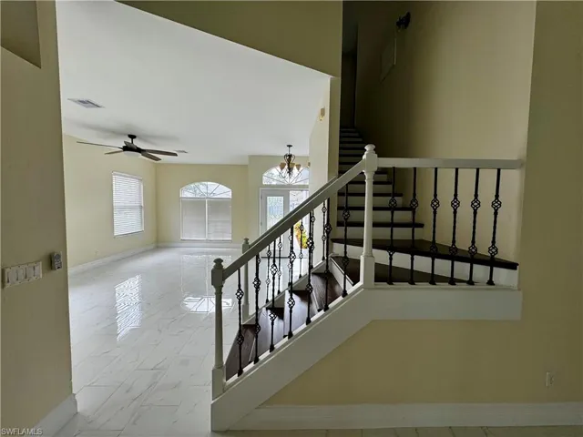 Stairs featuring baseboards, marble look tile flooring, a chandelier, and ceiling fan