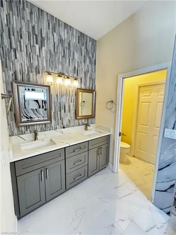 Full bathroom with an accent wall, toilet, marble finish flooring, baseboards, and double vanity