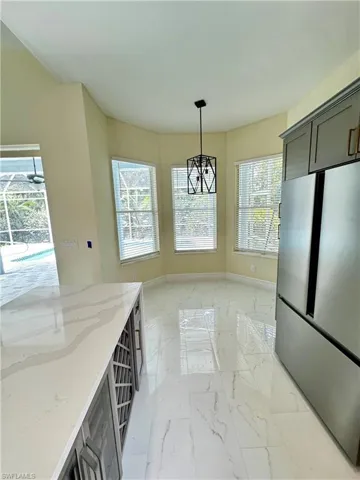 Kitchen with freestanding refrigerator, light marble finish flooring, light stone counters, pendant lighting, and baseboards