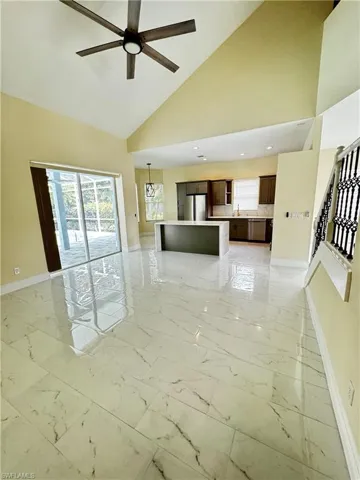 Unfurnished living room with baseboards, light marble finish floors, ceiling fan, stairway, and high vaulted ceiling
