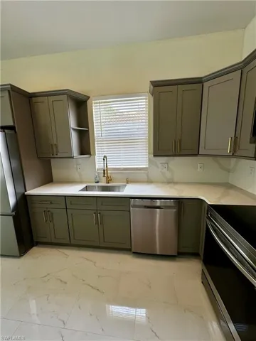Kitchen featuring appliances with stainless steel finishes, a sink, light marble finish floors, and light countertops