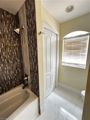 Full bath with marble look tiles, bathtub / shower combination, toilet, and baseboards