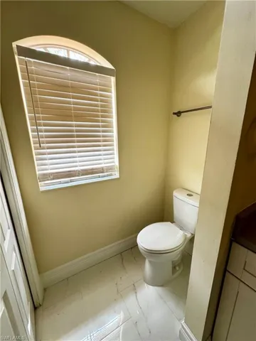 Half bath featuring marble finish flooring, toilet, and baseboards