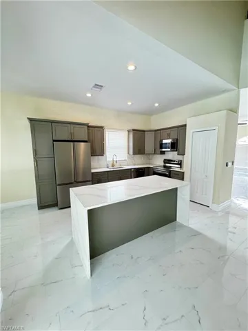 Kitchen featuring appliances with stainless steel finishes, a sink, a center island, baseboards, and recessed lighting