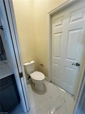 Bathroom featuring marble look tile flooring, toilet, and baseboards