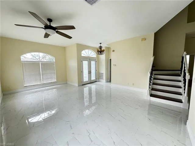 Unfurnished living room featuring light marble finish flooring, baseboards, stairs, and french doors