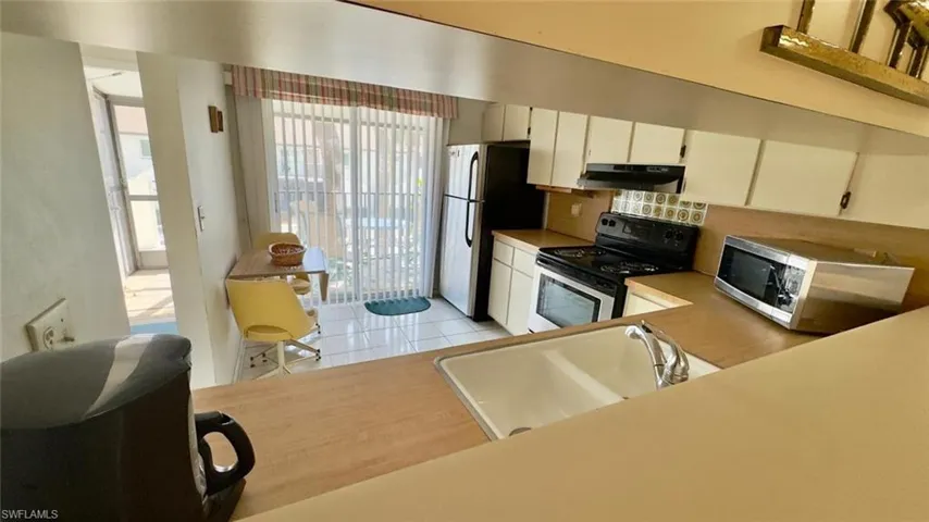 Kitchen featuring backsplash, sink, light tile patterned floors, stainless steel appliances, and white cabinets