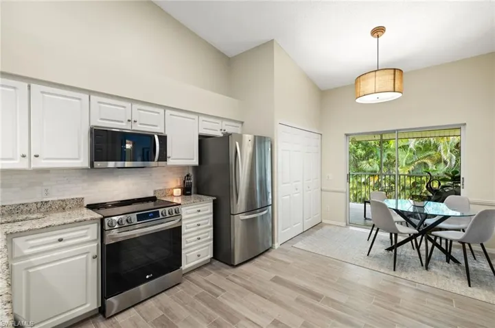 Kitchen featuring stainless steel appliances, decorative backsplash, white cabinets, high vaulted ceiling, and light wood-type flooring