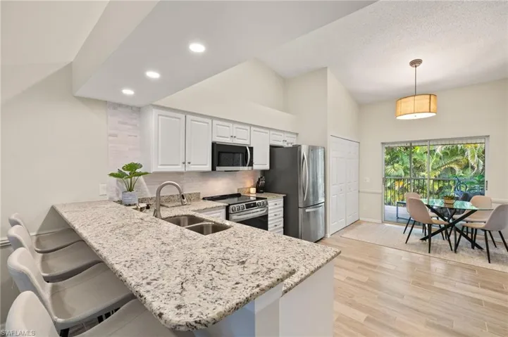 Kitchen featuring stainless steel appliances, light stone countertops, light wood-style floors, tasteful backsplash, and a peninsula