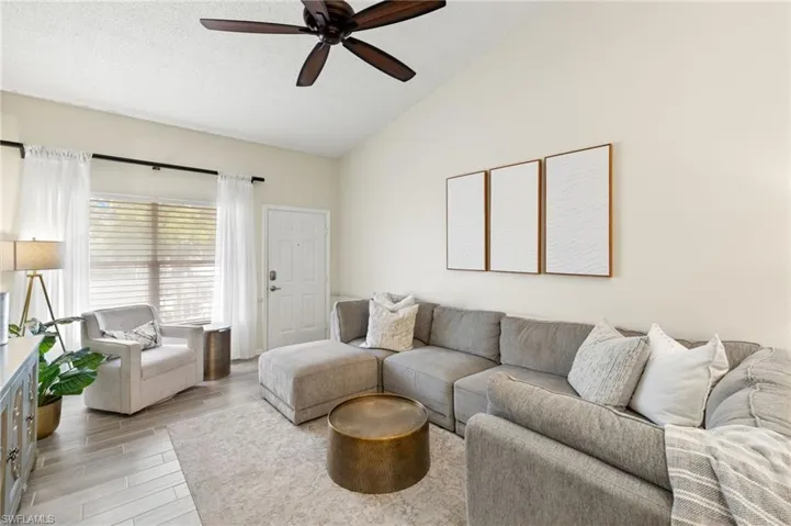 Living room with vaulted ceiling, a ceiling fan, light wood-style flooring, and a textured ceiling