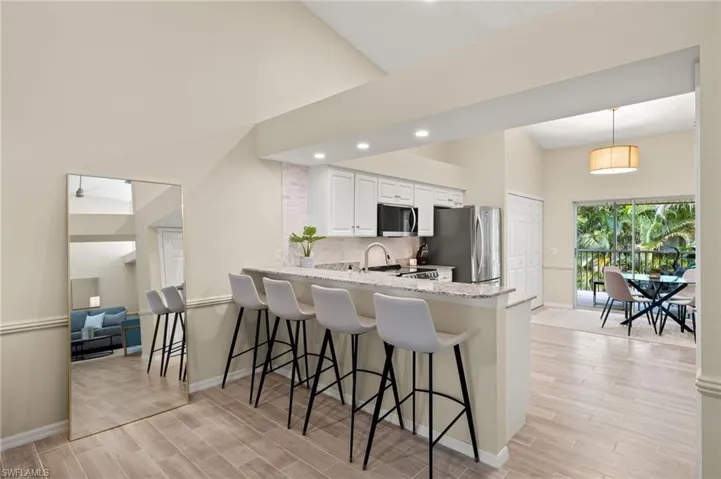 Kitchen featuring freestanding refrigerator, high vaulted ceiling, a peninsula, light stone counters, and light wood-style flooring
