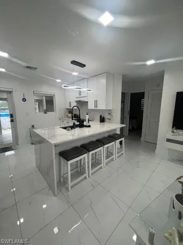 Kitchen featuring a breakfast bar, light stone counters, white cabinets, a peninsula, and hanging light fixtures