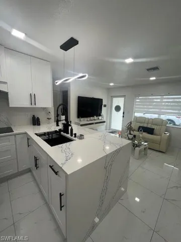 Kitchen featuring open floor plan, light marble finish flooring, and white cabinetry