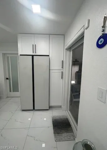Kitchen featuring light marble finish flooring, freestanding refrigerator, white cabinets, and a textured wall