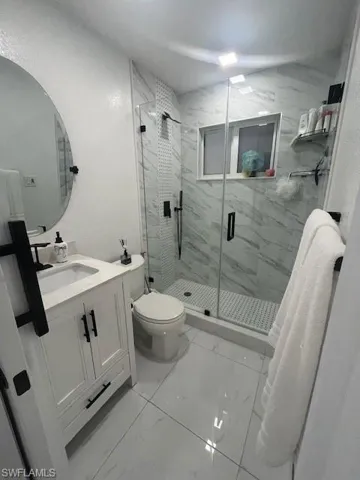 Bathroom with a marble finish shower, light marble finish flooring, vanity, and a textured wall