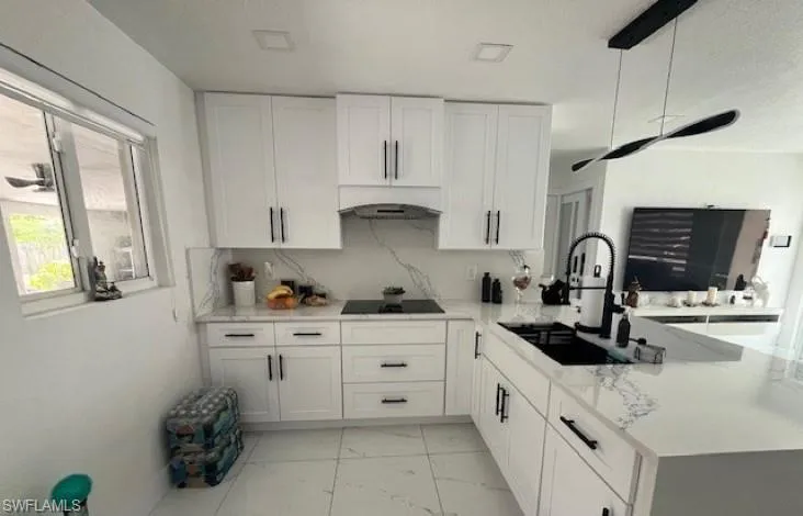 Kitchen with white cabinets, light marble finish flooring, a peninsula, and light stone counters